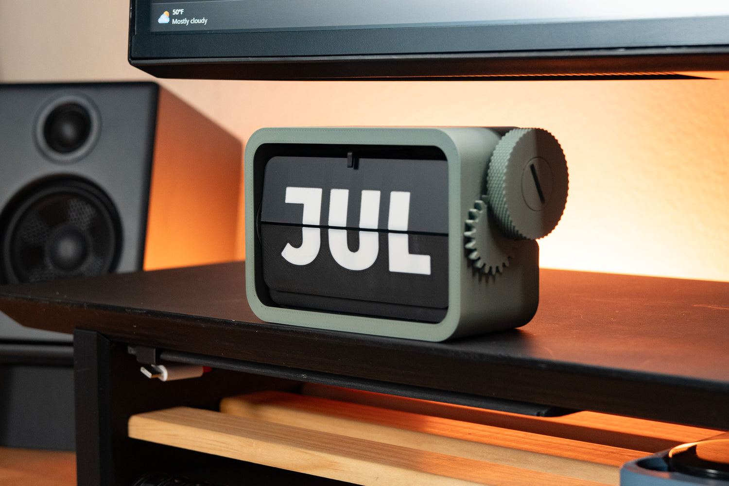 3d printed flip calendar with green body and white on black lettering sitting on desk shelf.  